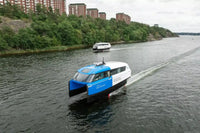Candela P-12 Blue and white ferry boat on a river with greenery and buildings in the background