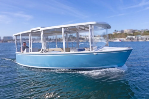 Blue Duffy Balboa 20 Electric Boat with a white canopy on a body of water with a clear sky.