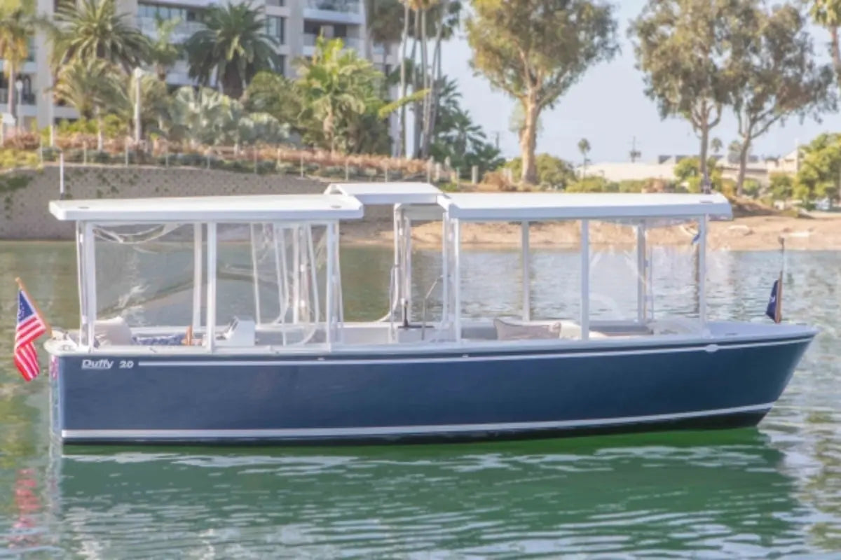 Duffy Balboa 20  Blue and white boat on a body of water with trees and buildings in the background