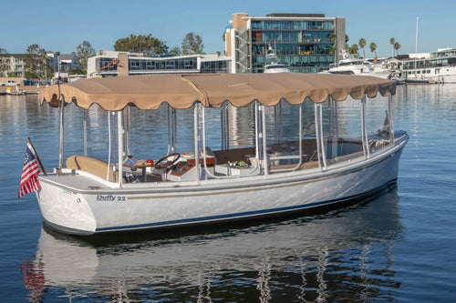 White Duffy Bay Island 22 Electric Boat with a canopy on a body of water with buildings in the background