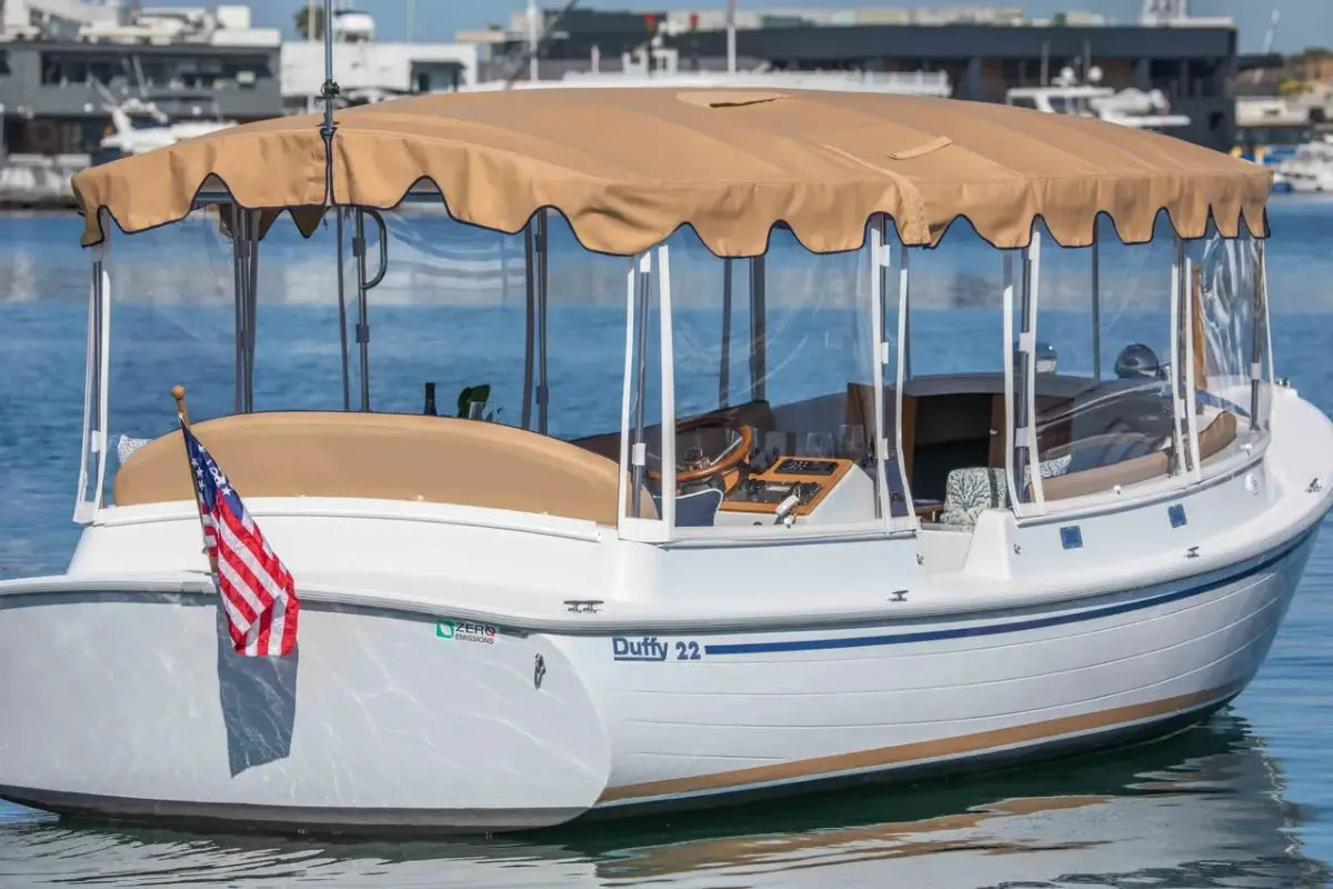 Duffy Cuddy Cabin 22 Electric Boat with a tan canopy on a body of water, featuring an American flag.