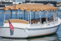 Duffy Cuddy Cabin 22 Electric Boat with a tan canopy on a body of water, featuring an American flag.