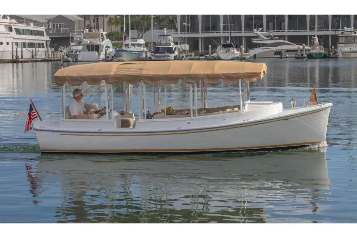 Duffy Cuddy Cabin 22 Electric Boat with a canopy on a body of water with buildings in the background
