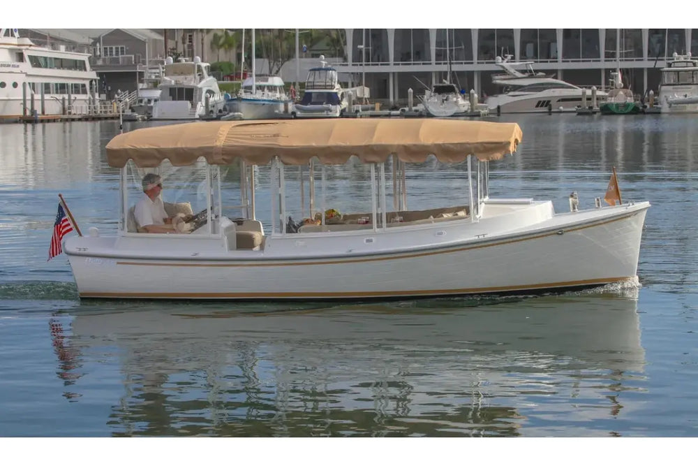 Duffy Cuddy Cabin 22 Electric Boat with a canopy on a body of water with buildings in the background