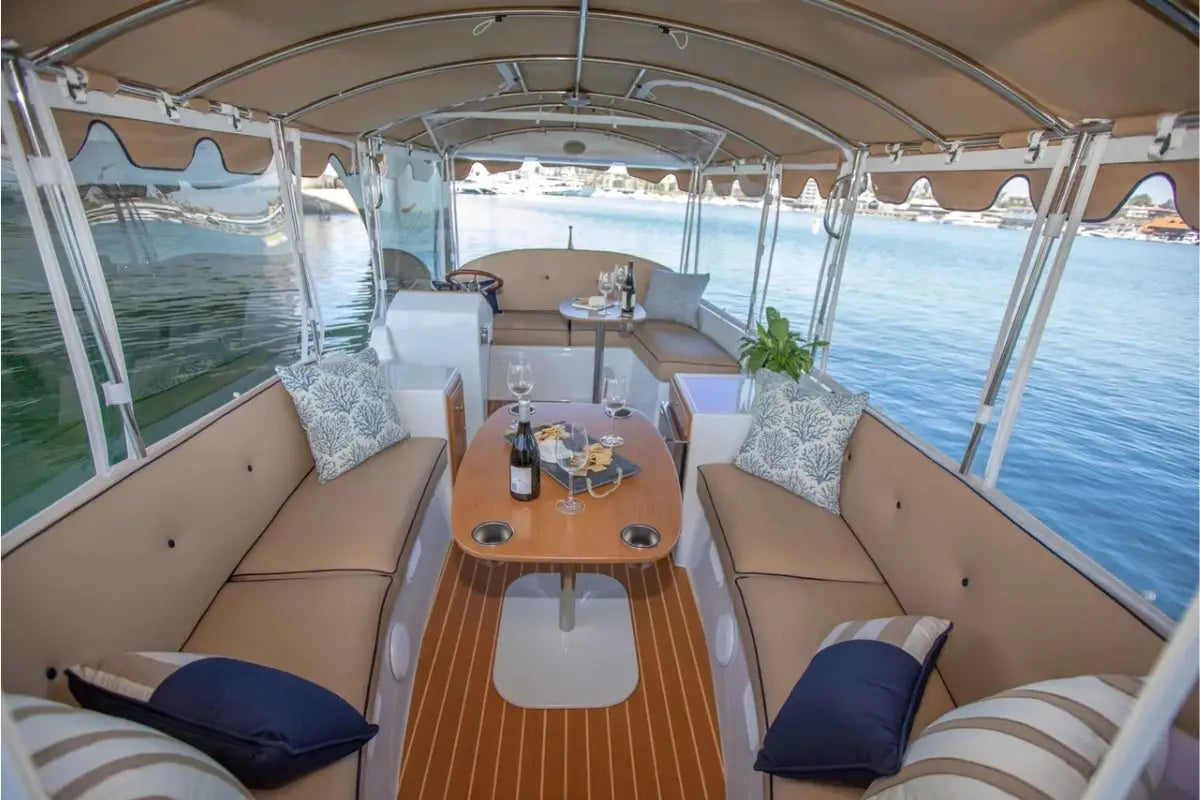 Interior of a Duffy Cuddy Cabin 22 Electric Boat with beige seating, wooden table, and water view