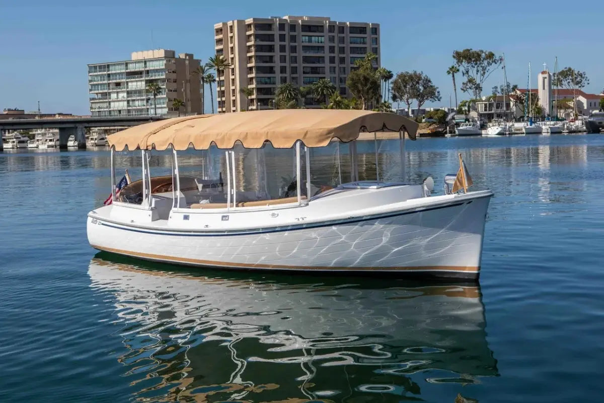 Duffy Cuddy Cabin 22 Electric Boat with a canopy on a calm body of water with buildings in the background