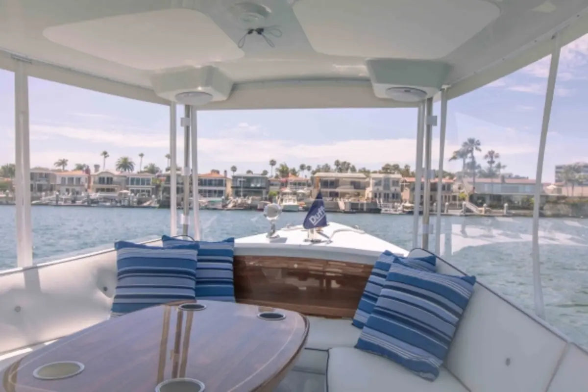 Interior of Duffy Sun Cruiser 23 Electric Boat with blue and white striped cushions, table, and view of water and buildings.