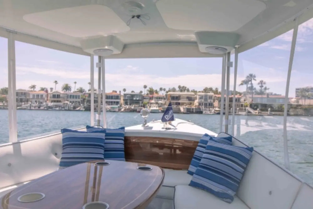 Interior of Duffy Sun Cruiser 23 Electric Boat with blue and white striped cushions, table, and view of water and buildings.