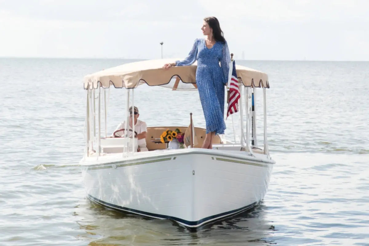 Woman in a blue dress standing on Duffy Sun Cruiser 23 Electric Boat with a canopy, on a body of water.