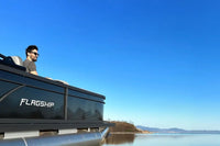 Man sitting on a Flux Flagship Discover Electric Boat on a calm lake with clear blue sky.