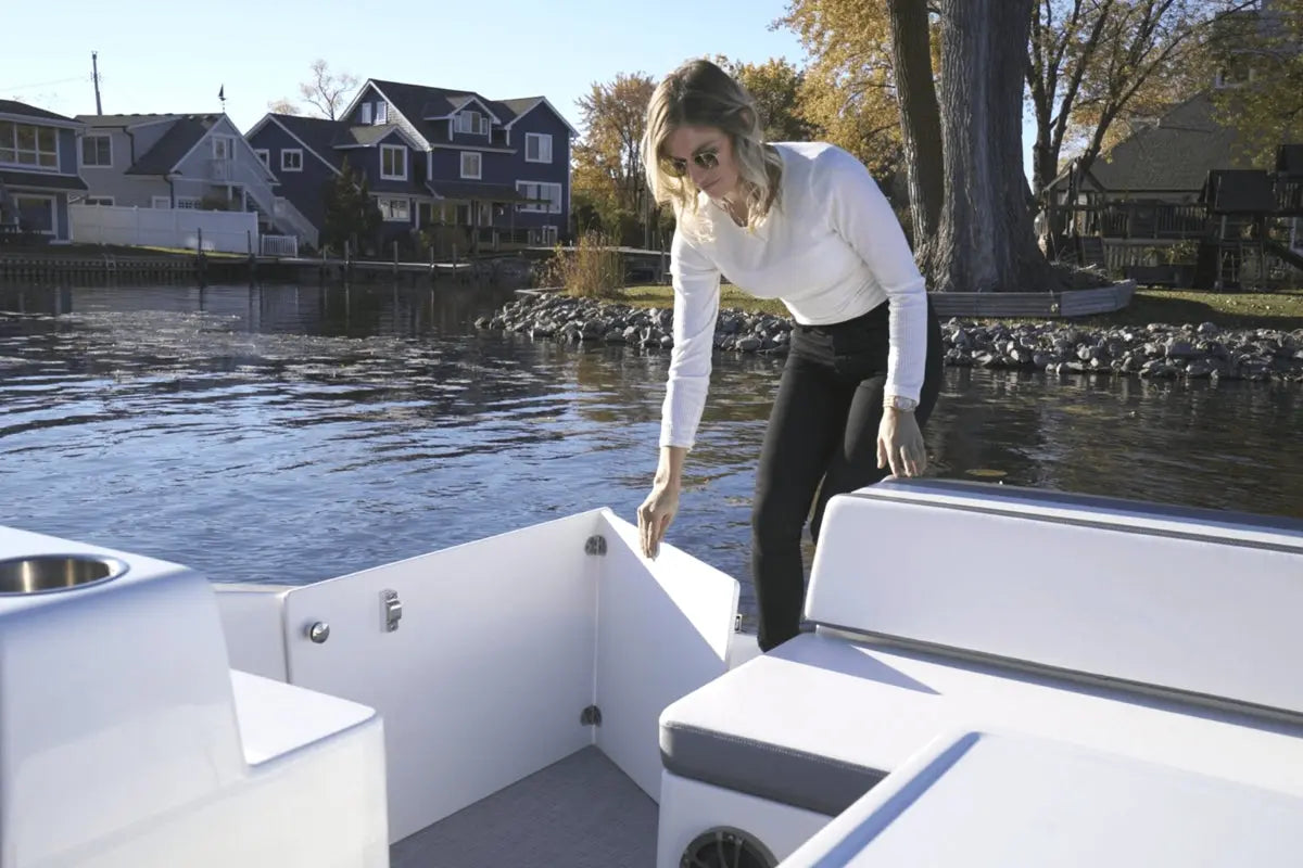 Woman standing on Flux GFX Stealth Electric Catamaran Boat by a waterfront with houses and trees in the background