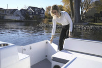 Woman standing on Flux GFX Stealth Electric Catamaran Boat by a waterfront with houses and trees in the background