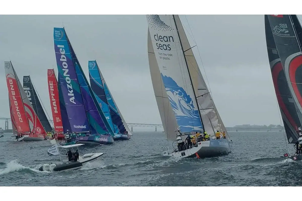 Sailboats racing on a body of water with various brands' names on their sails.