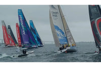 Sailboats racing on a body of water with various brands' names on their sails.