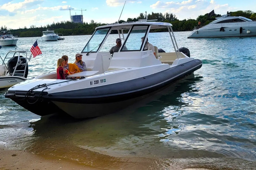White inflatable Hyfoil 32 Electric Boat on a sandy beach with people around, surrounded by other boats and greenery.
