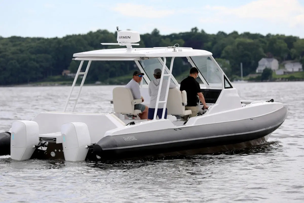White inflatable Hyfoil 32 Electric Boat on water with people onboard, surrounded by trees and houses.