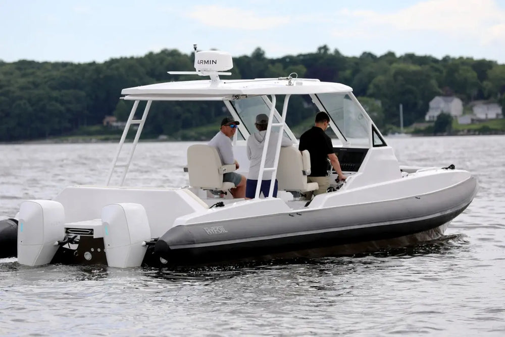 White inflatable Hyfoil 32 Electric Boat on water with people onboard, surrounded by trees and houses.