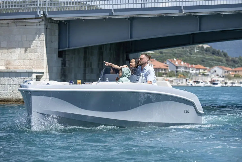 Two people on Rand Breeze 20 Electric Boat in the water with a bridge and buildings in the background