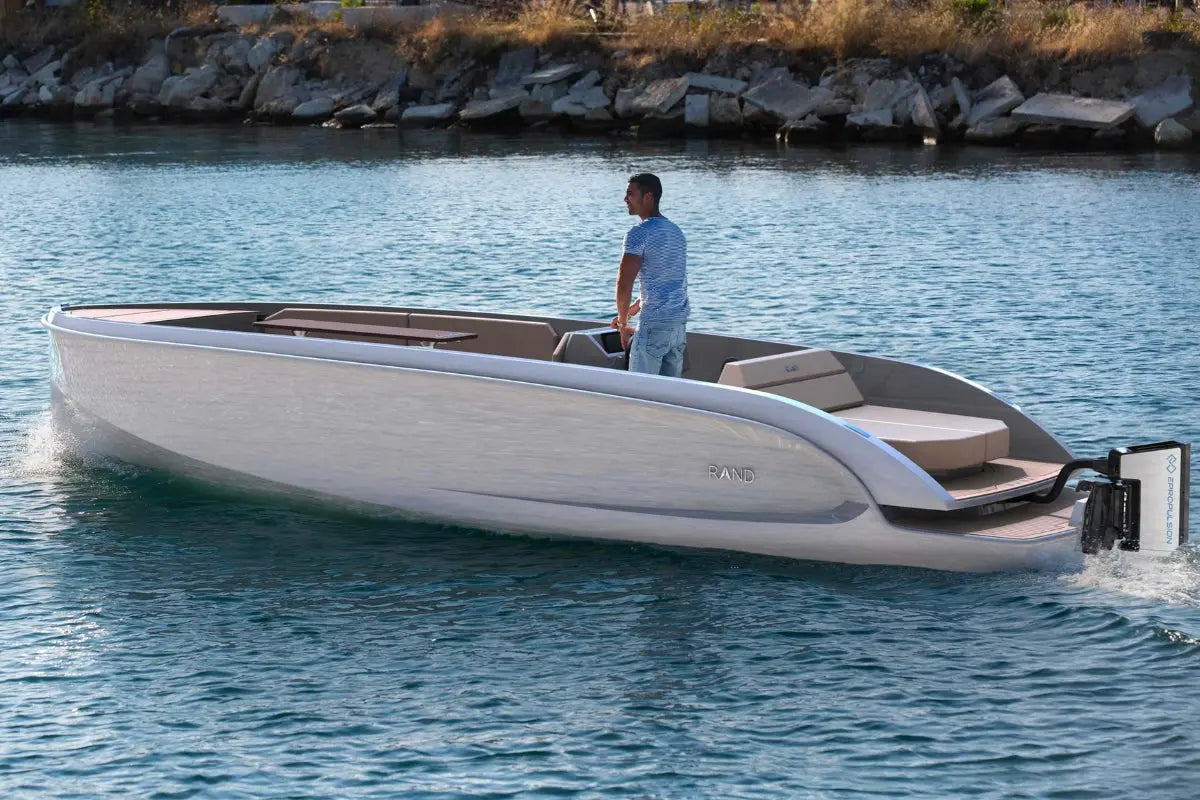 Man standing on a modern Rand Mana 24 Electric Boat on a body of water.