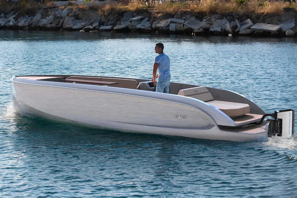 Man standing on a modern Rand Mana 24 Electric Boat on a body of water.