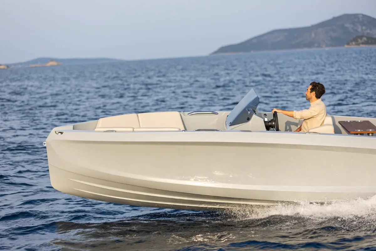 Person driving a white Rand Source 22 Electric Boat on a body of water with mountains in the background