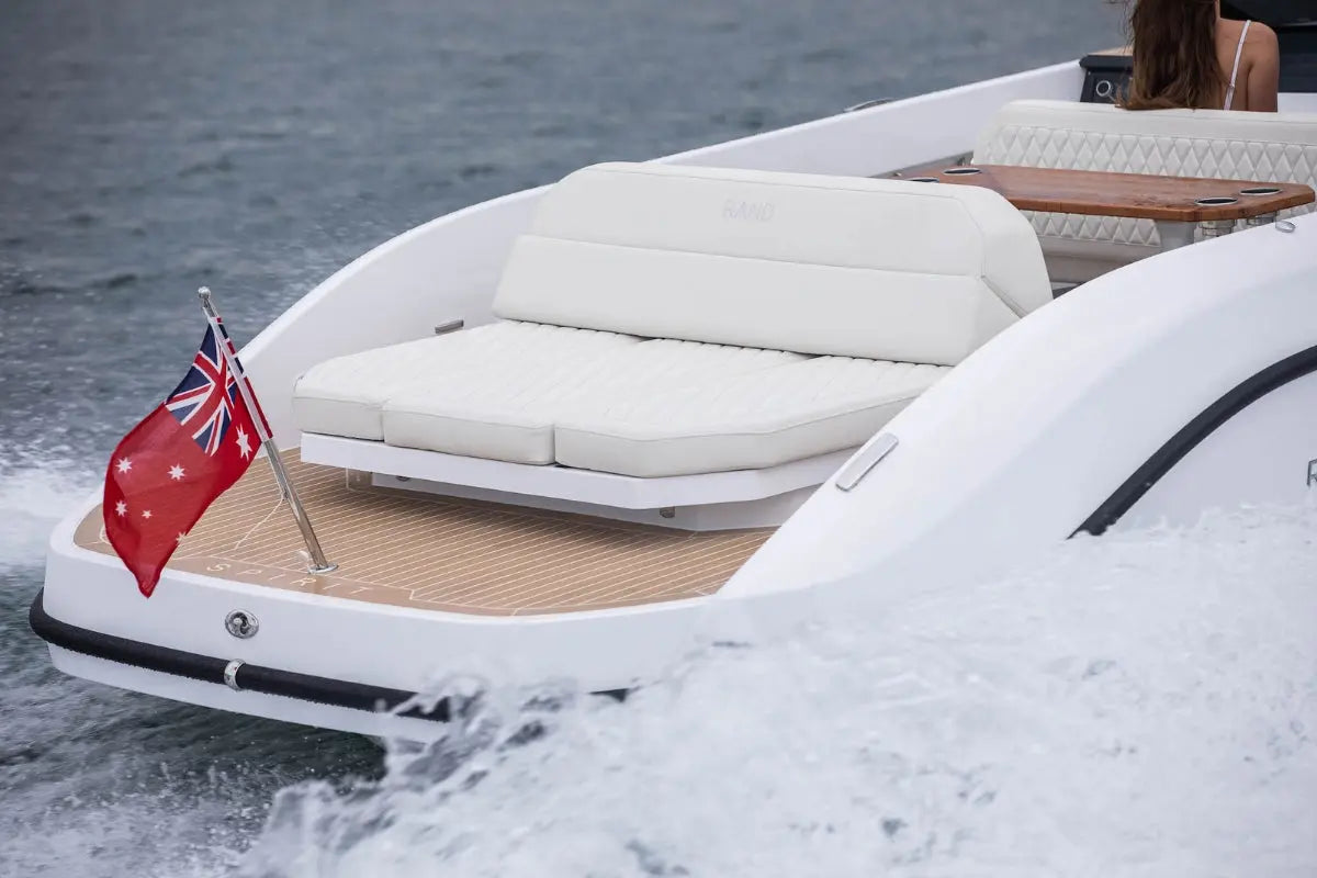Rand Spirit 25 Electric Boat with cushioned seating area and a flag on a body of water