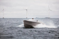 Rand Spirit 25 Electric Boat speeding on water with wind turbines in the background