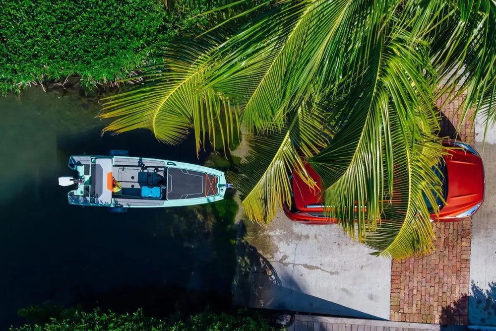 Veer V13 Electric Boat docked by a red car under palm trees with a river in the background