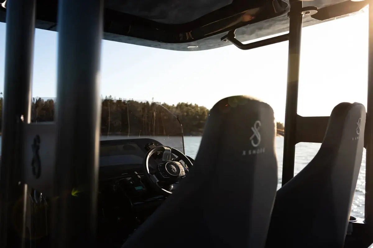 X Shore Pro Electric Boat interior with steering wheel and seats, facing a sunset over water.
